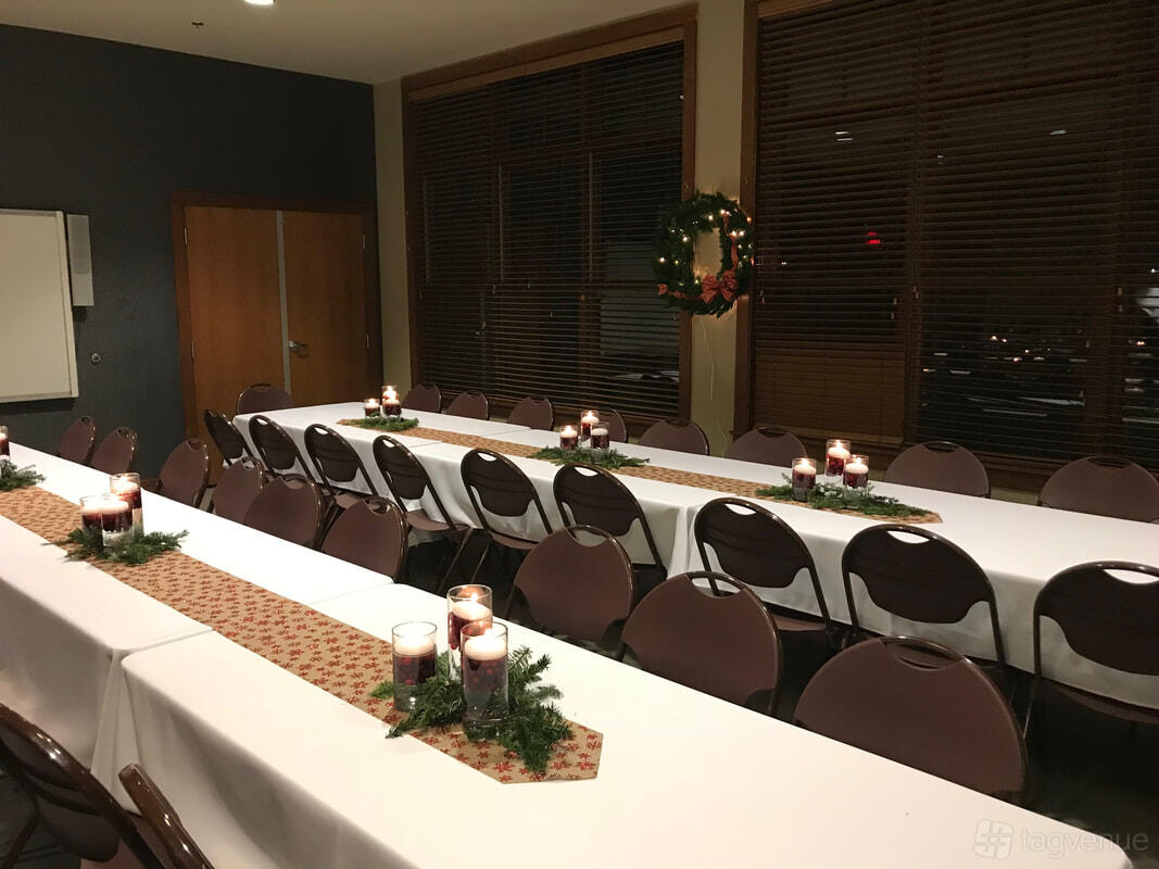 An event venue with rectangular tables covered in white linens, holiday wreath, and candle centerpieces at Zilker Lodge.