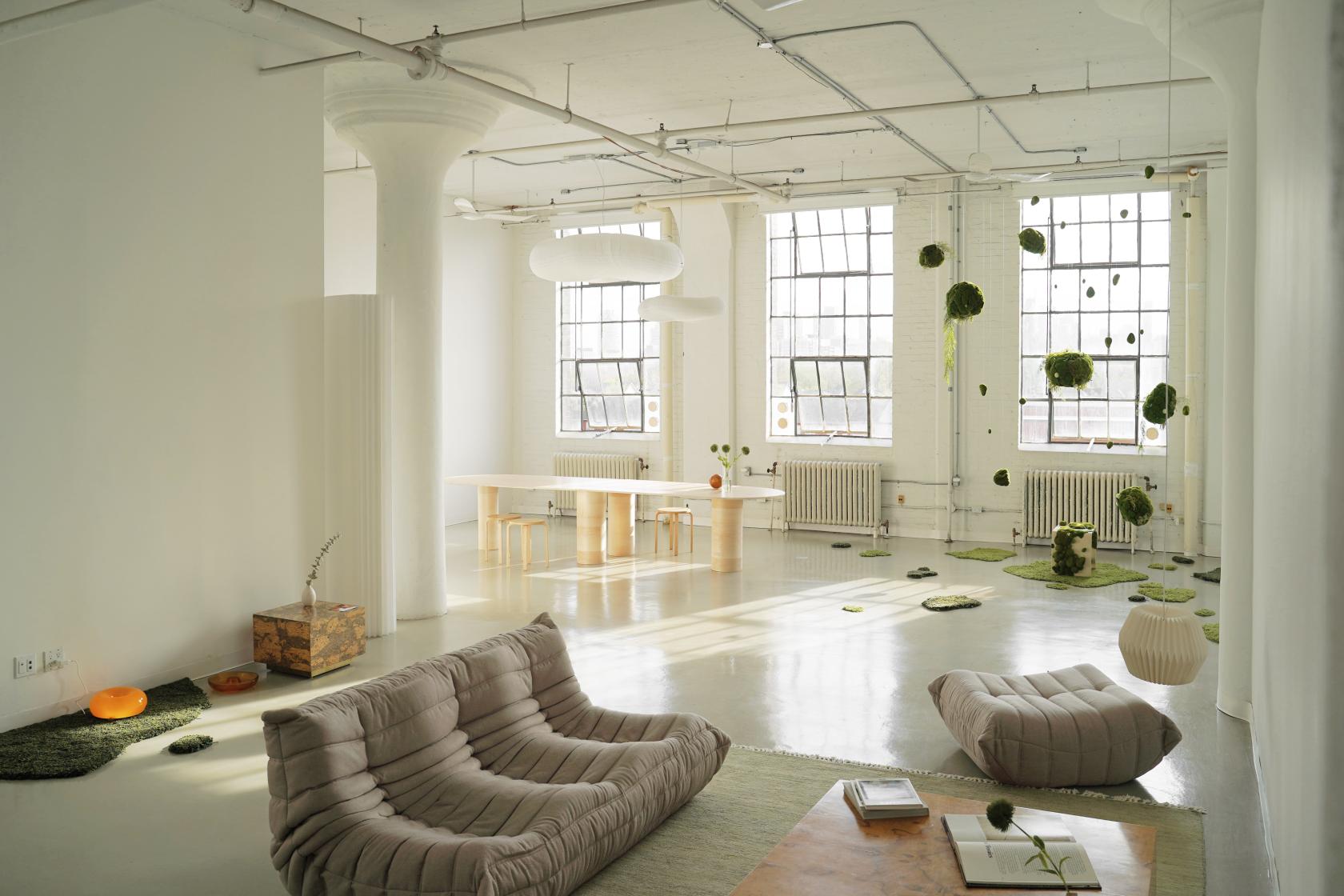 A gallery with high ceilings, large industrial windows, minimalist seating, and hanging greenery at New York Style Studio Loft & Event Space.