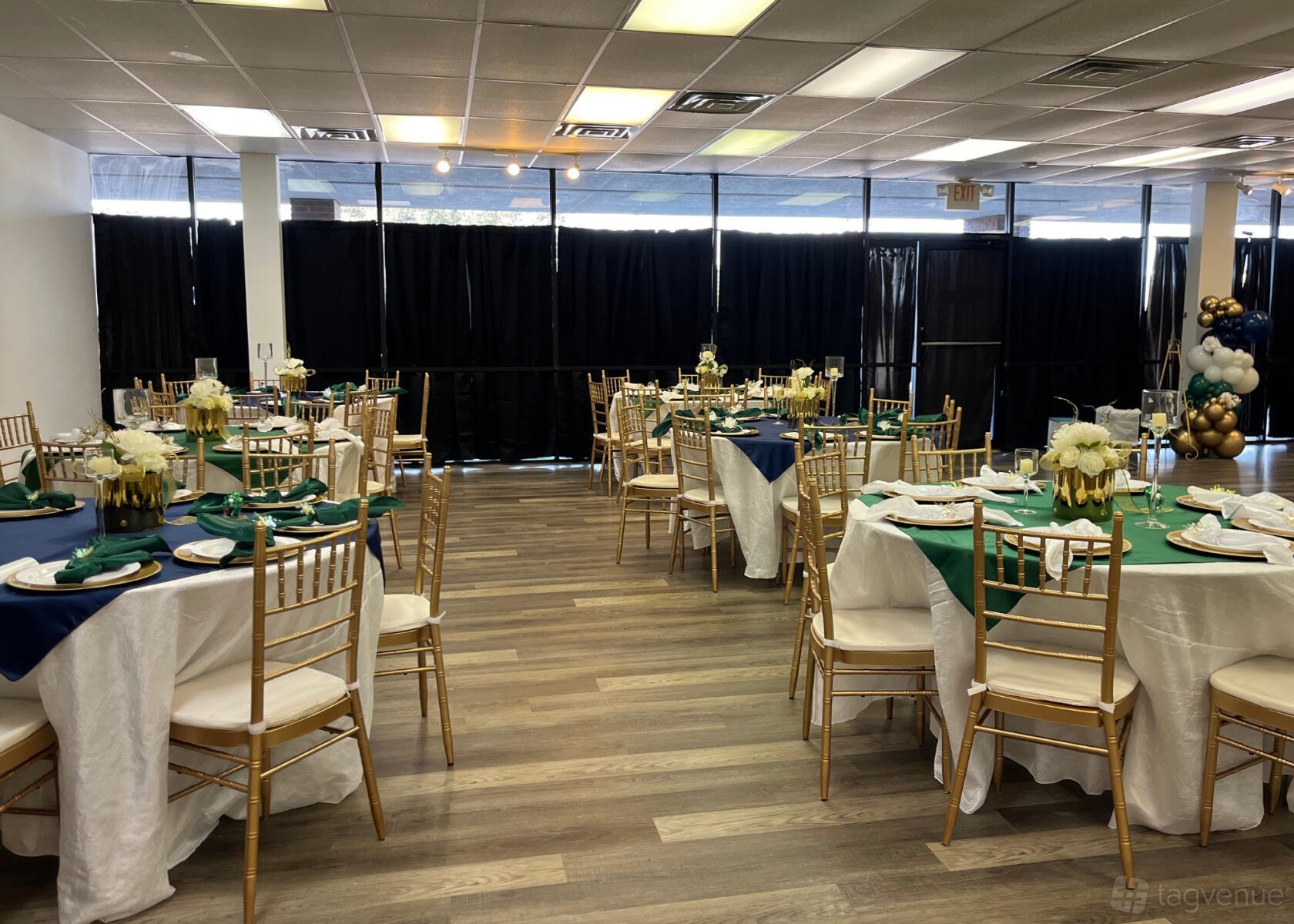 An event venue with round tables dressed in white linens, gold chairs, and floral centerpieces at Easy Celebrations.