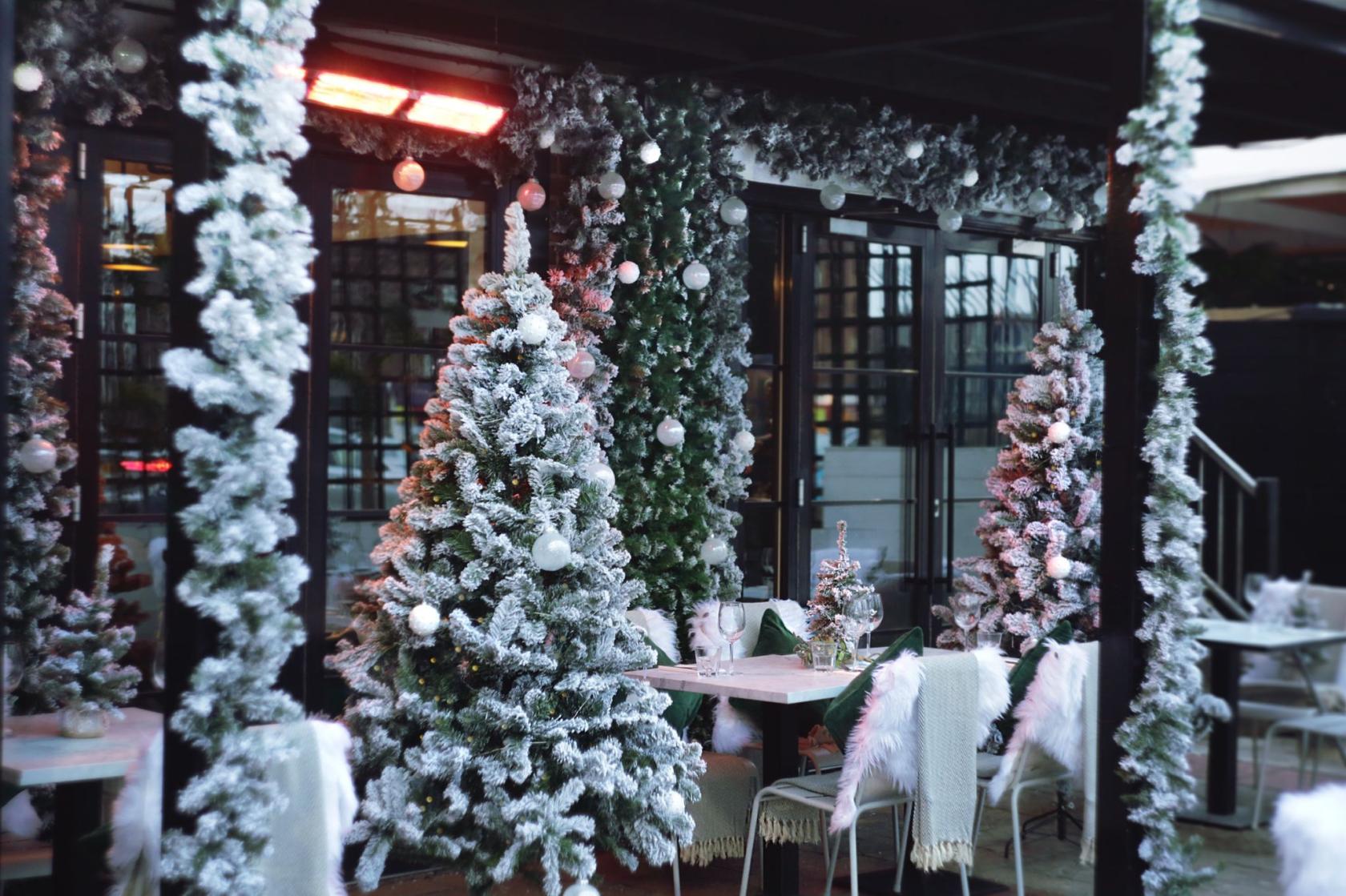 A cocktail bar decorated with snow-covered Christmas trees and white ornaments on the patio at Exhibit.