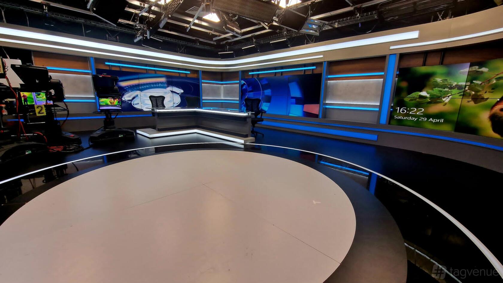 A TV studio with a circular stage, broadcast desk, multiple cameras, and LED lighting at Vision Studios.