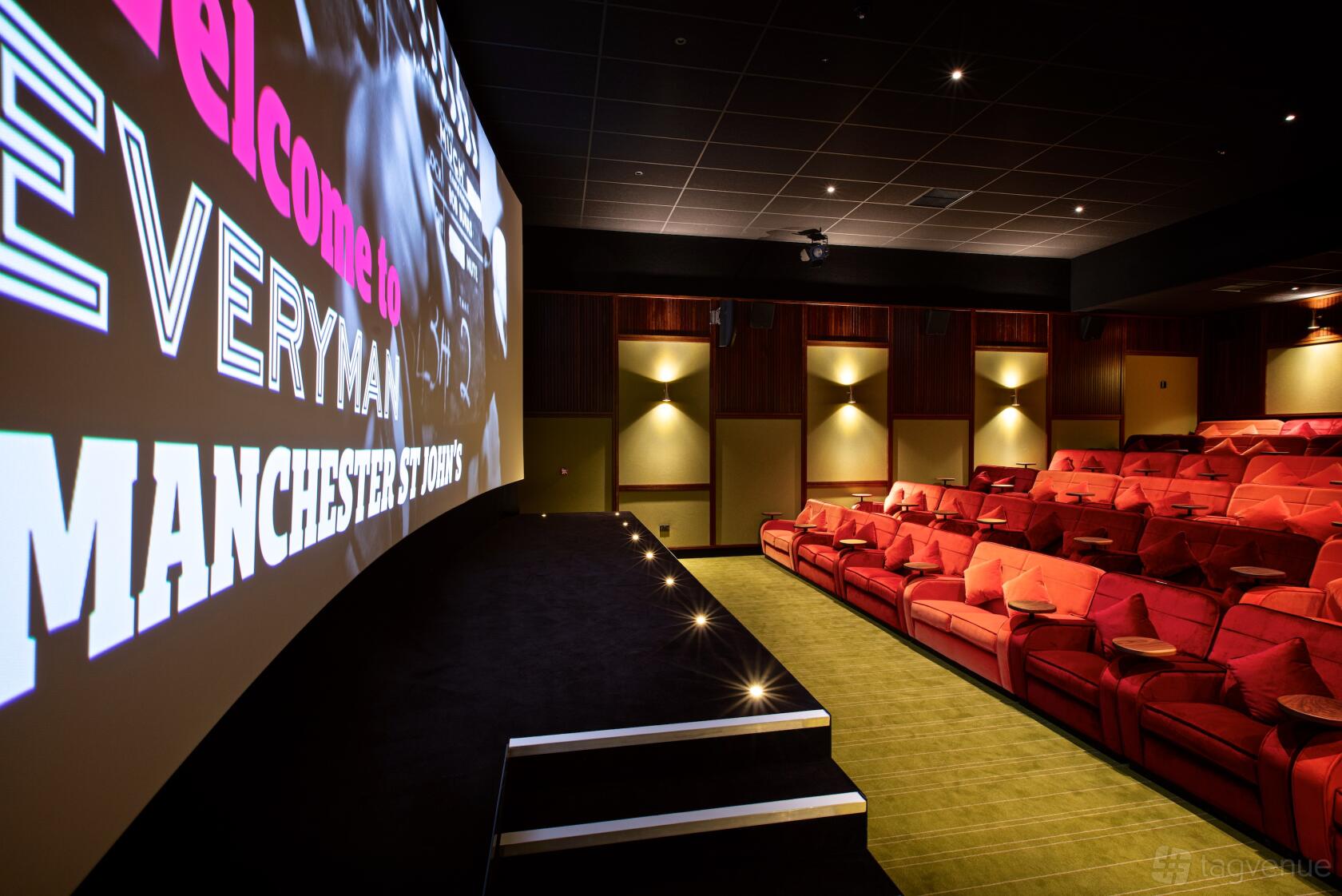 A screening room with plush red armchairs, carpeted floors, and a large projection screen at Everyman Manchester St Johns.