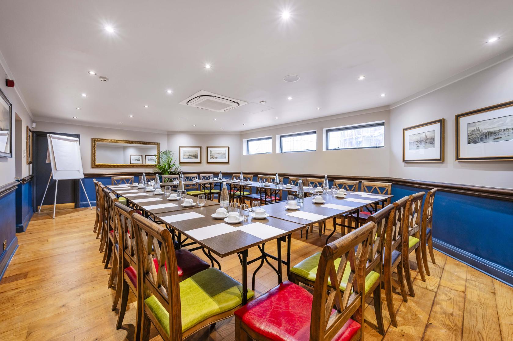 A boardroom in a pub with wooden floors, U-shaped tables set for a meeting, and framed prints on the walls at Doggett's Coat and Badge.