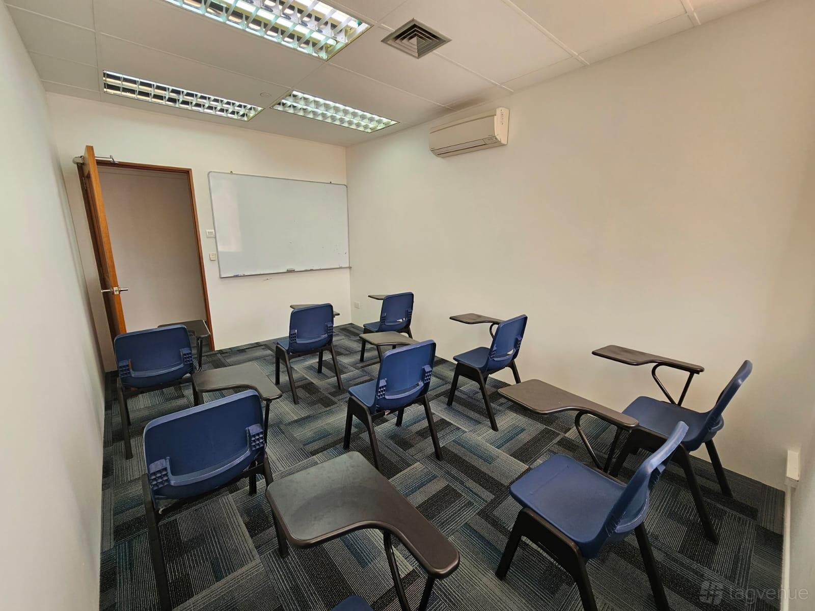 A meeting centre room with blue chairs with writing tablets, a whiteboard, and fluorescent lighting at Vislas Academy.