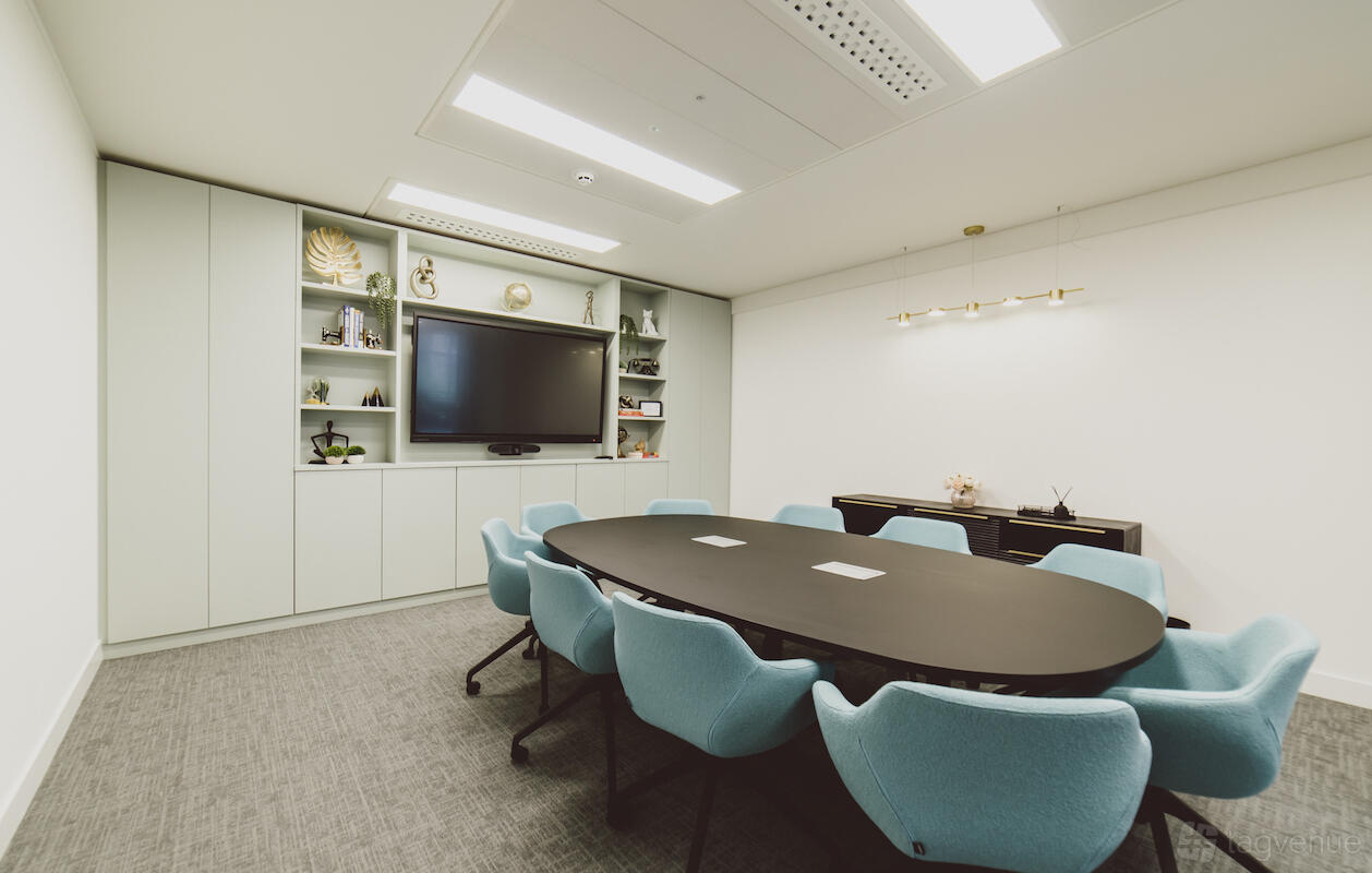 A meeting centre with a large oval table, light blue chairs, built-in shelving, and a wall-mounted screen at Orega Manchester Arkwright House.