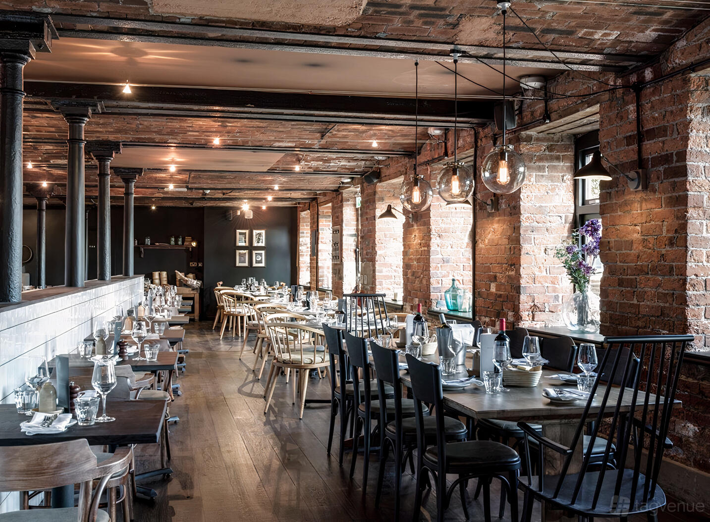 A restaurant with exposed brick walls, industrial lighting, and wooden tables set for dining at Brasserie Blanc Leeds.