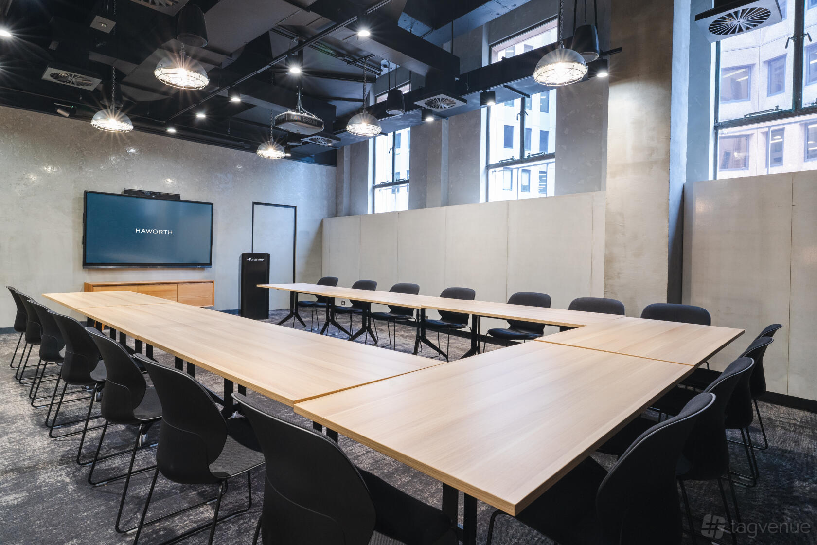 A meeting room with U-shaped wooden tables, black chairs, large windows, and ceiling-mounted lights at The Porter.