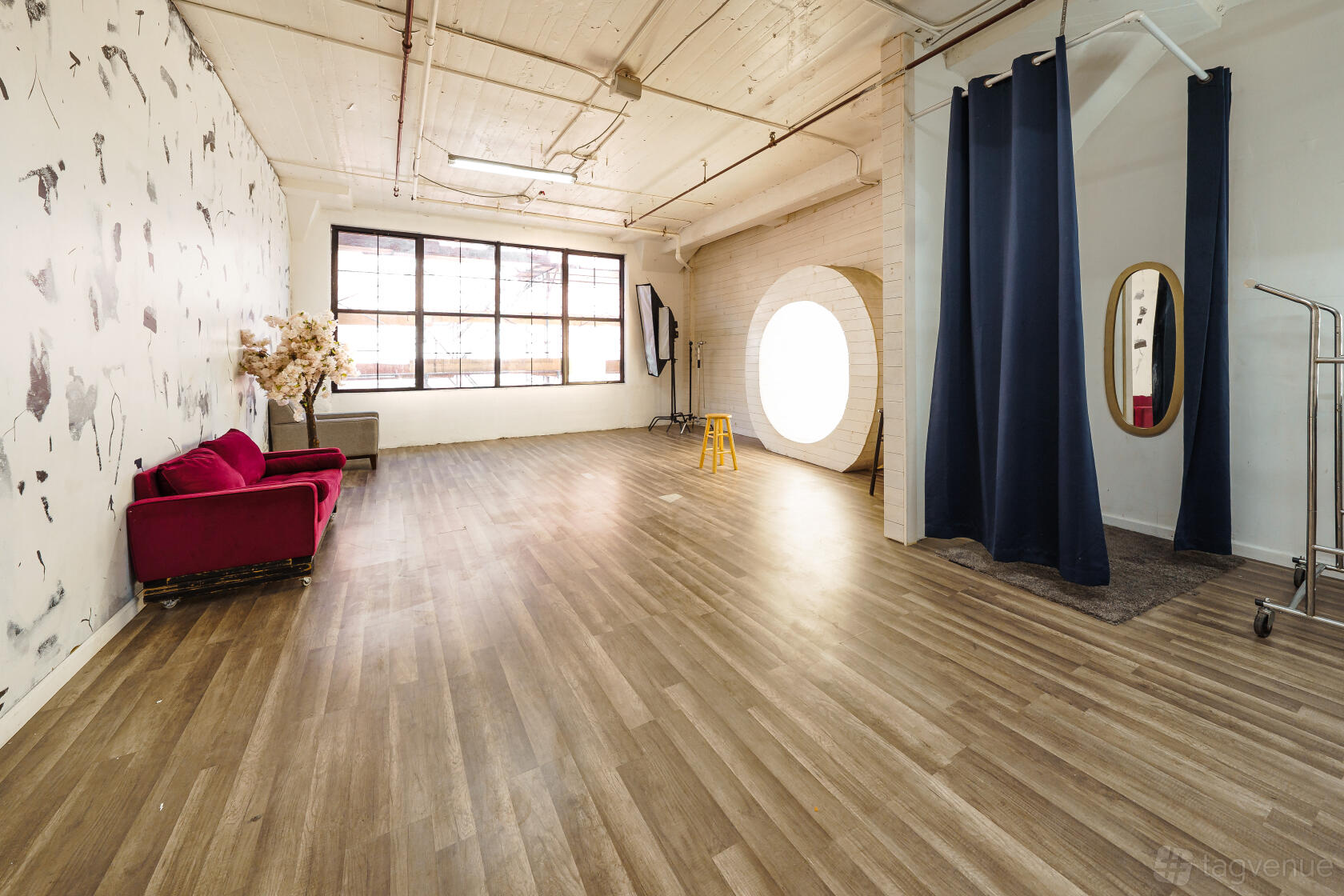 A photo studio with large industrial windows, wood floors, a red velvet sofa, and a round light at N.Y. Studios.
