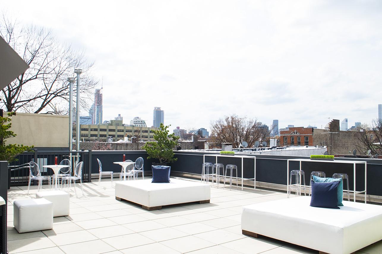 A rooftop venue with white lounge seating, transparent bar stools, and skyline views at Melrose Ballroom.