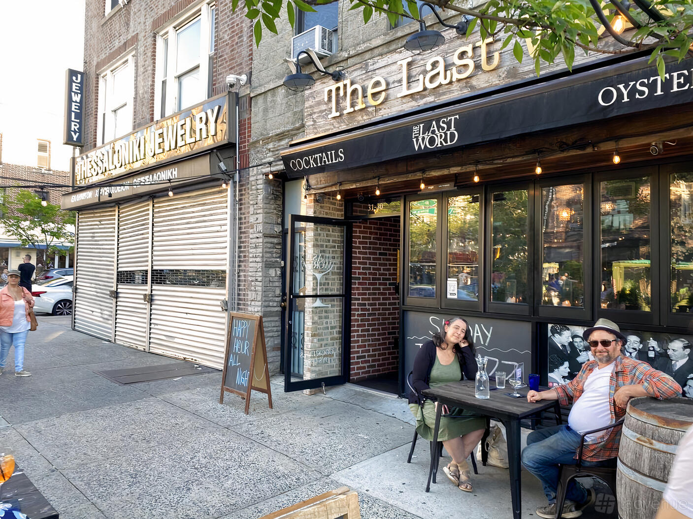 A pub with outdoor seating on a sidewalk, black-framed windows, and a barrel table at The Last Word