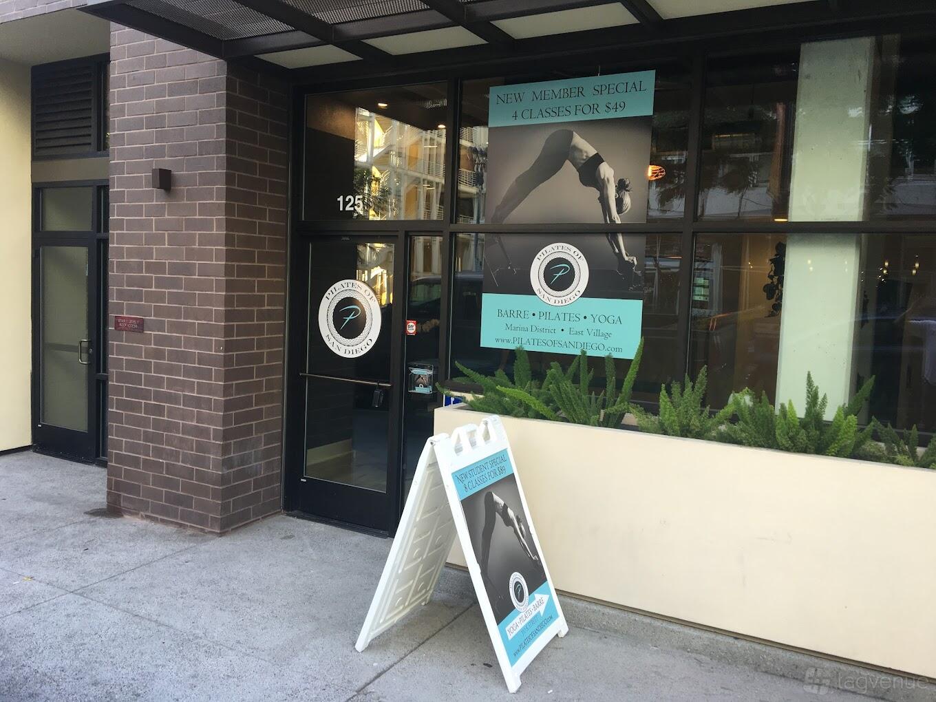 A dance studio entrance with floor-to-ceiling windows, brick accents, and A-frame signage at Pilates of San Diego - Downtown Location.