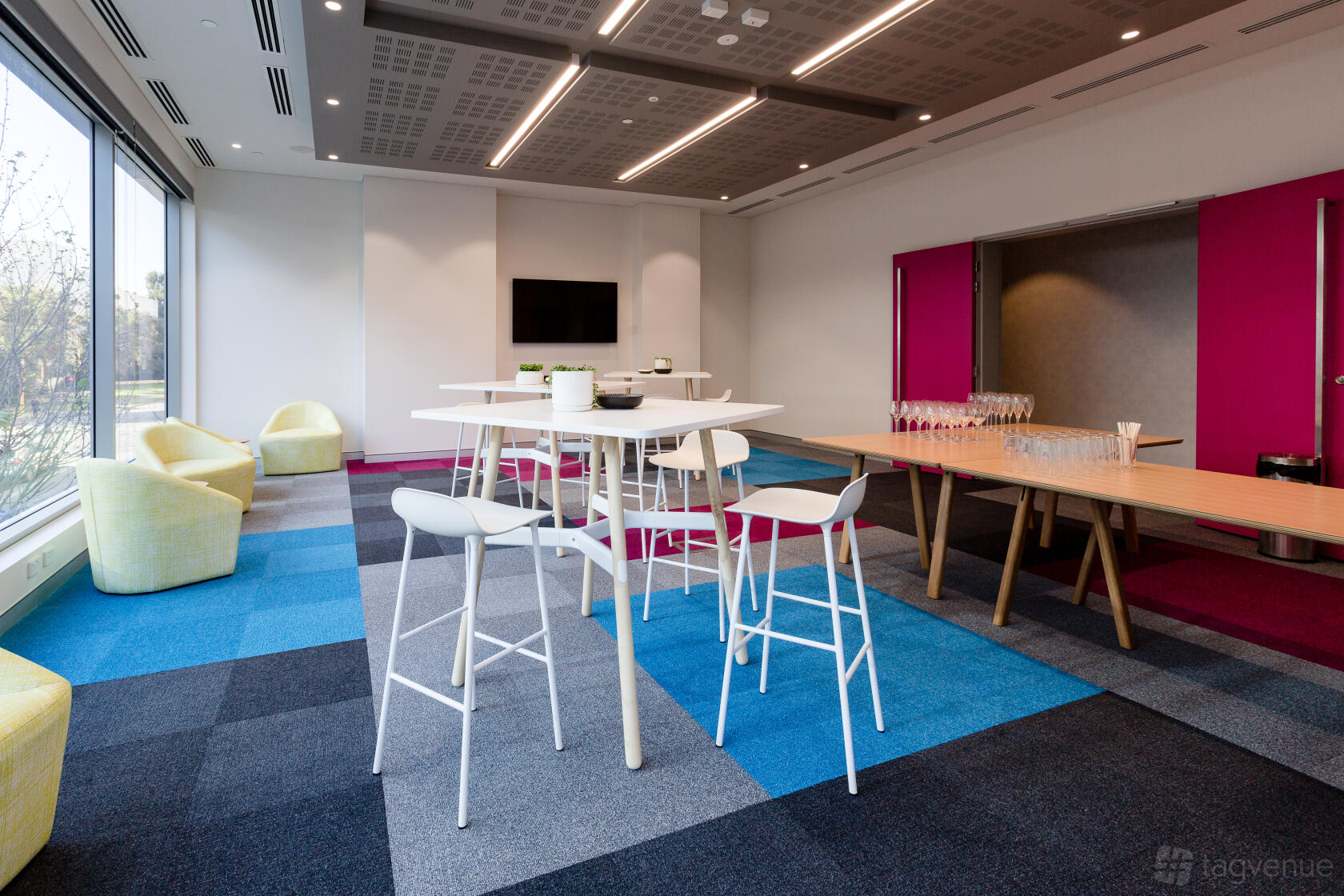 A function room with large windows, colorful carpet tiles, white high tables and chairs at ibis Styles East Perth.