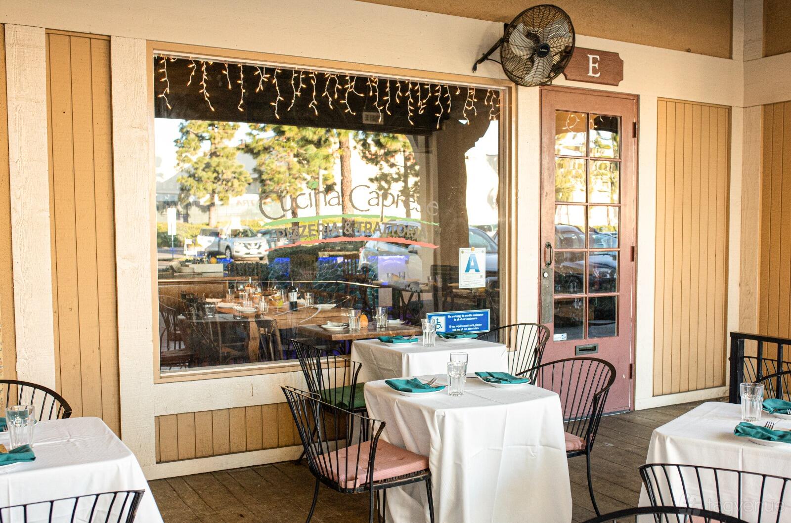 A restaurant patio with white tablecloths, teal napkins, black chairs, and string lights at Cucina Caprese Pizzeria & Trattoria.