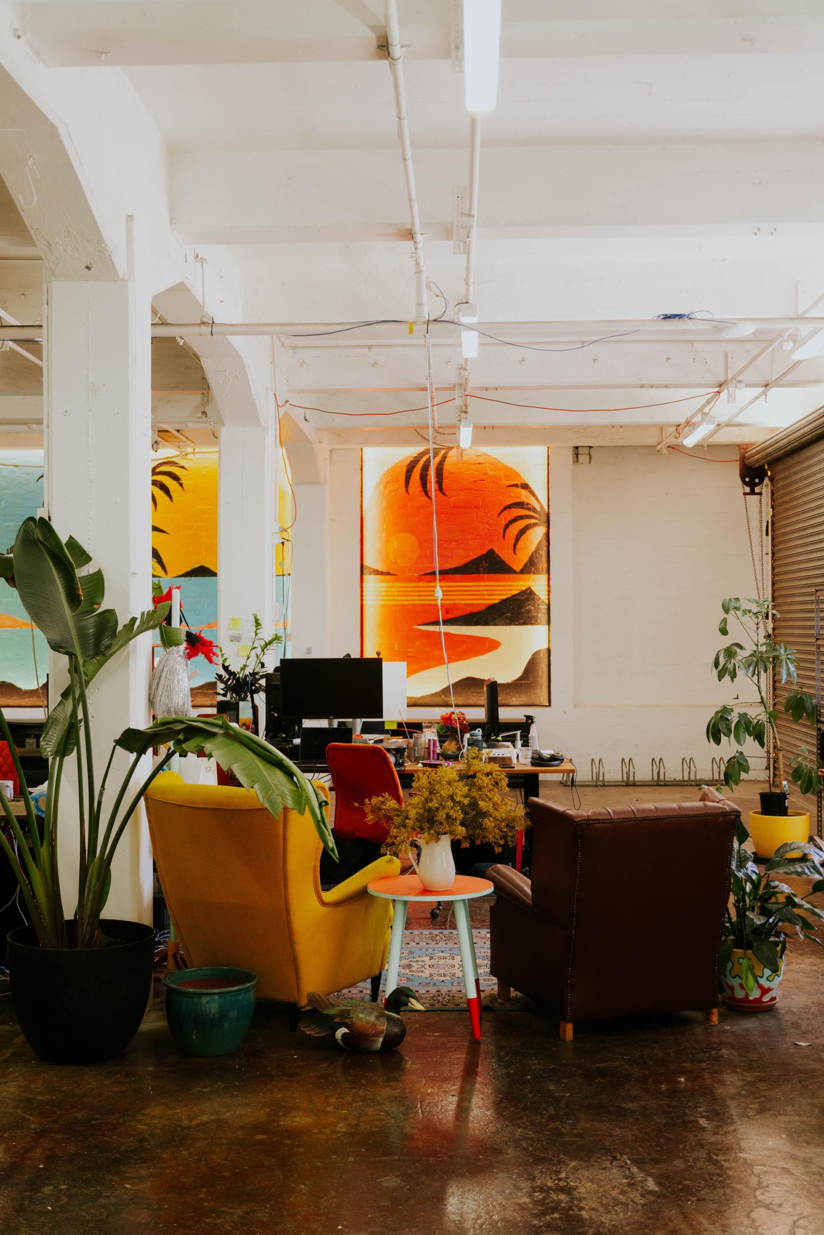 A coworking space with colorful chairs, large potted plants, and bright mural windows at CoParadiso.