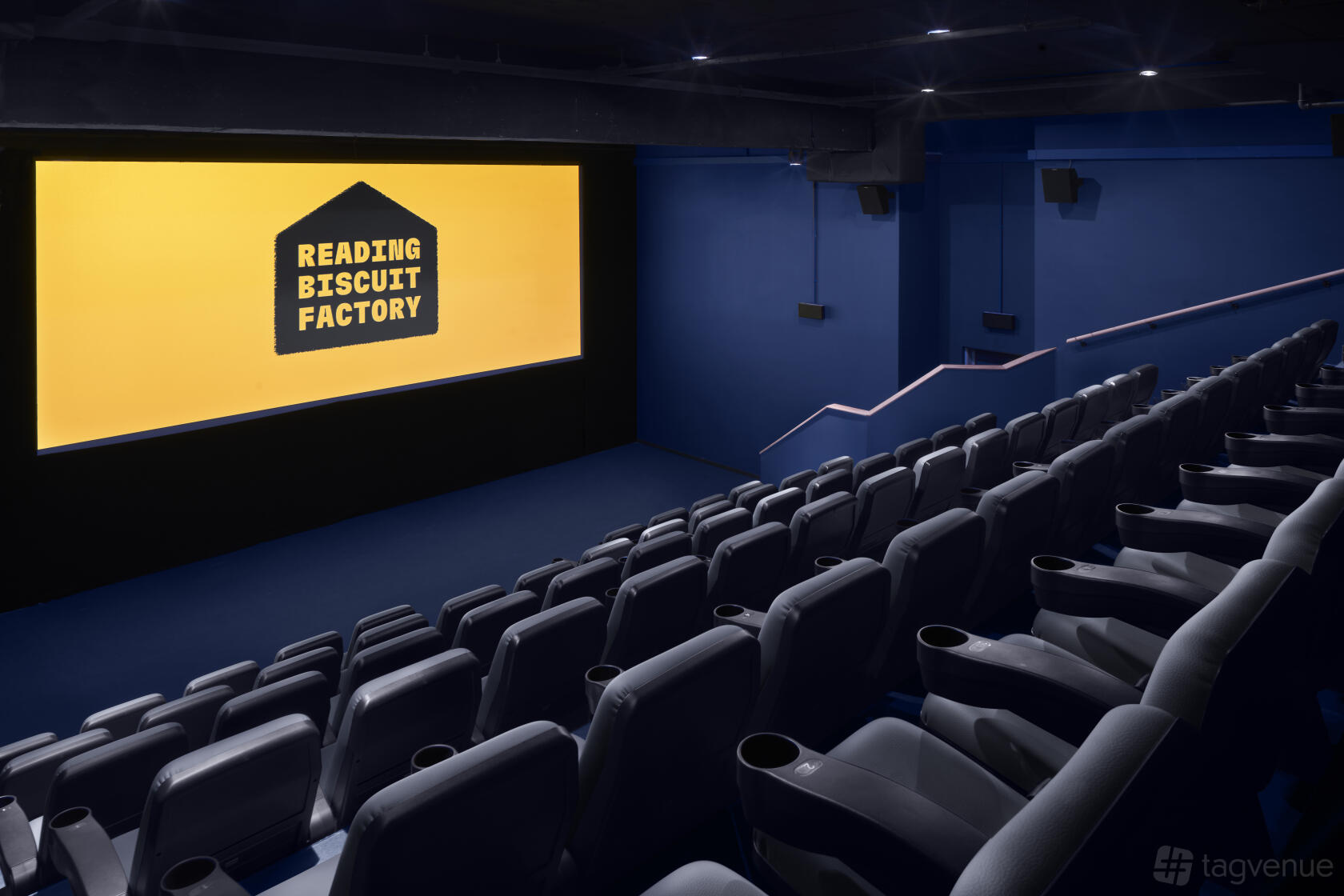 A cinema with tiered rows of black recliner seats facing a large screen at Reading Biscuit Factory.