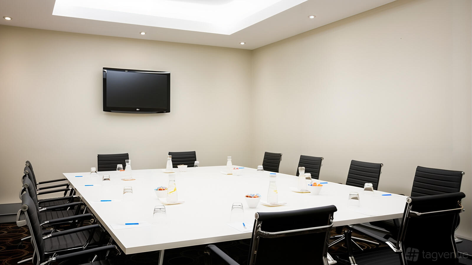 A hotel boardroom with a large rectangular table, black leather chairs, and a wall-mounted TV at Mantra Melbourne Airport.