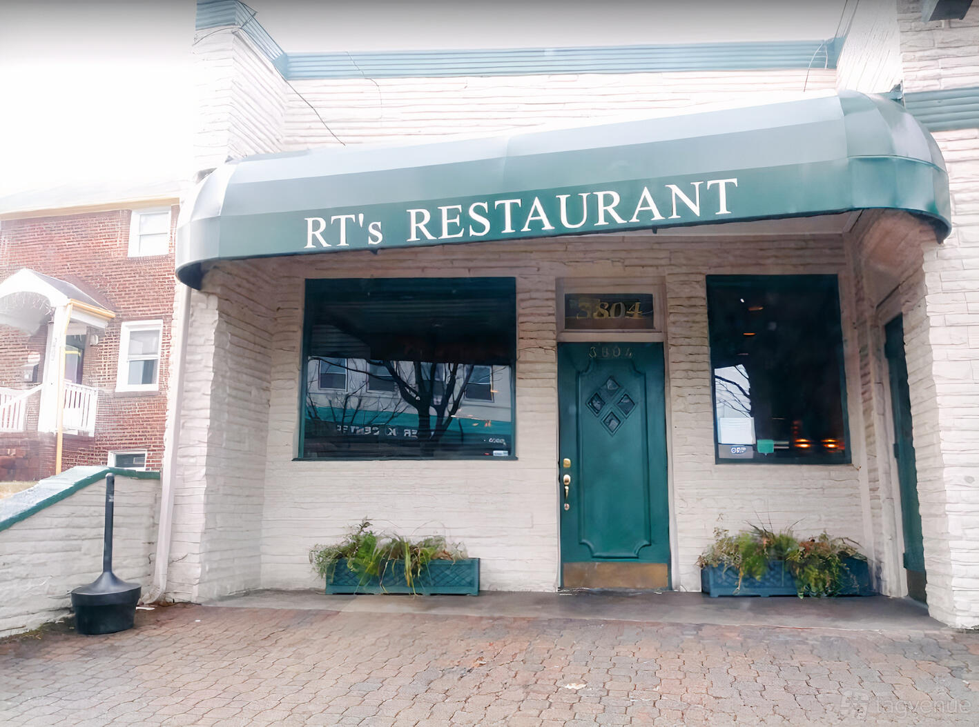 A restaurant with a green awning, large front windows, and potted plants at the entrance at RT's Restaurant.