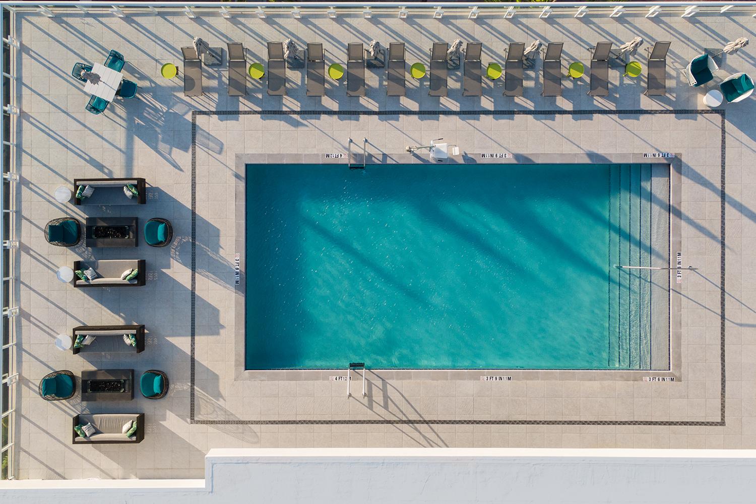 A hotel rooftop with a rectangular pool, lounge seating, and sun chairs at Courtyard Delray Beach.