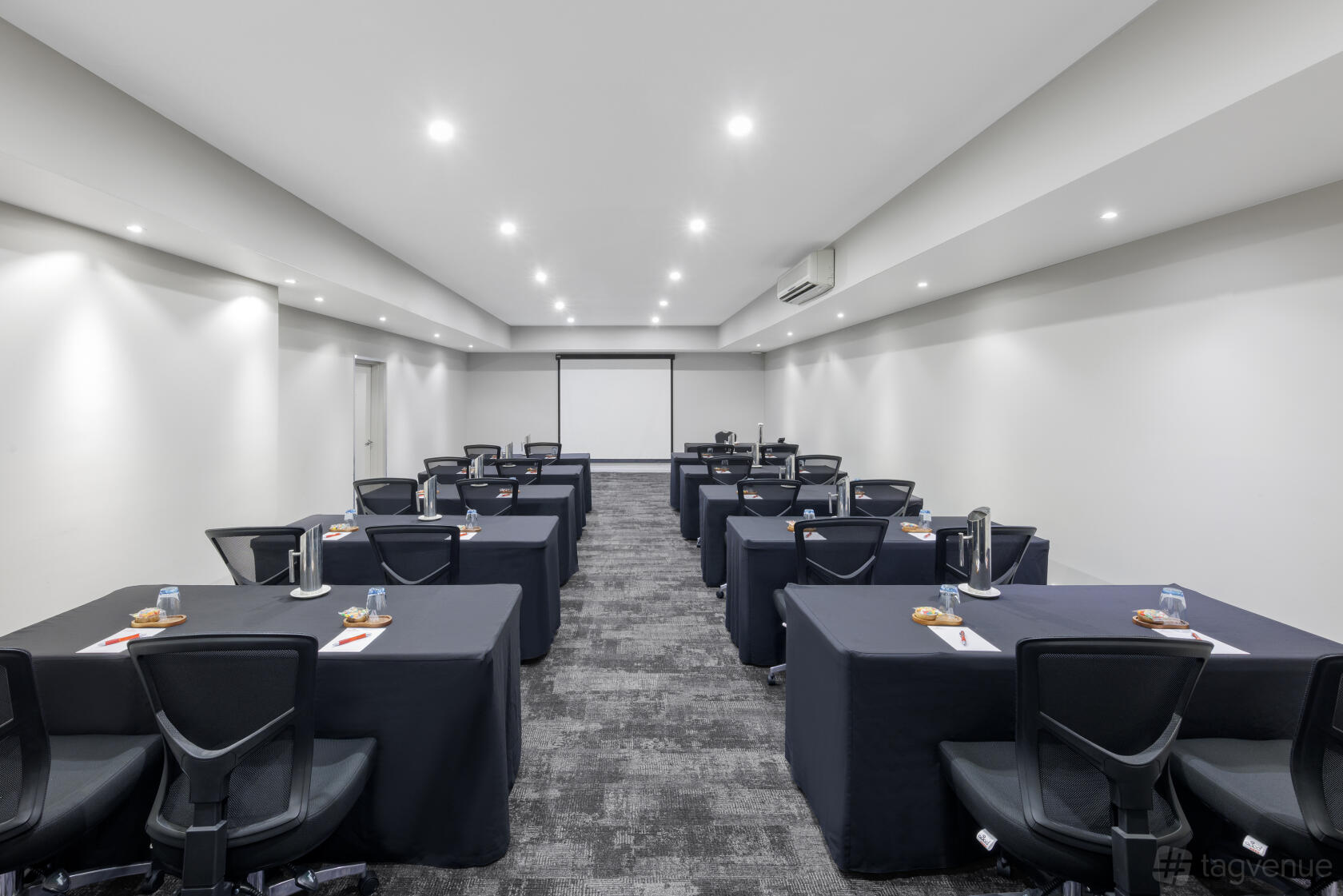 A hotel meeting room with rows of black-draped tables, ergonomic chairs, and ceiling spotlights at Hotel Grand Chancellor Melbourne.