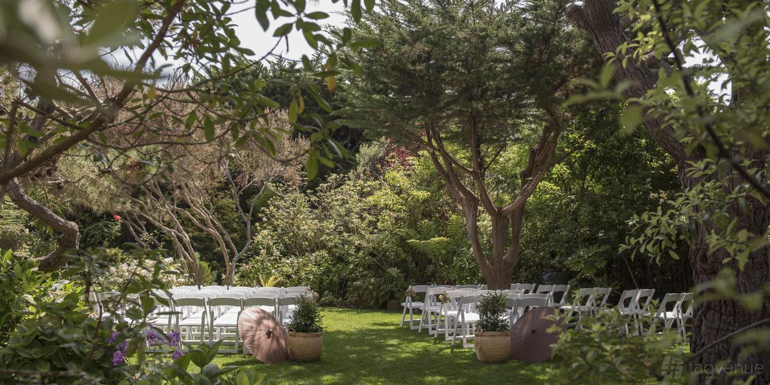 A garden ceremony site with white folding chairs on green lawn surrounded by mature trees at Hastings House Weddings.