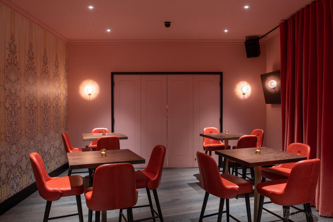 An event venue room with pink walls, red upholstered chairs, wooden tables, and wall sconces at Puttshack Bank.