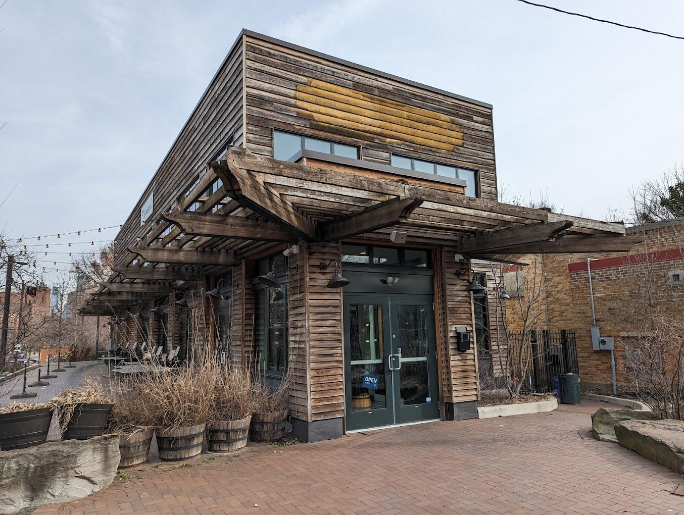 A restaurant with weathered wood siding, large windows, and a pergola-covered entrance at Renata's Kitchen.