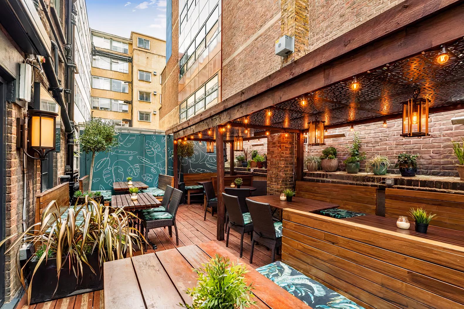 A pub terrace with wooden decking, string lights, potted plants, and covered seating at Carpenters Arms.