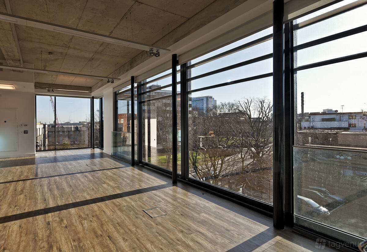 A hall with floor-to-ceiling windows, wood flooring, and exposed concrete ceiling at Osmani Centre.