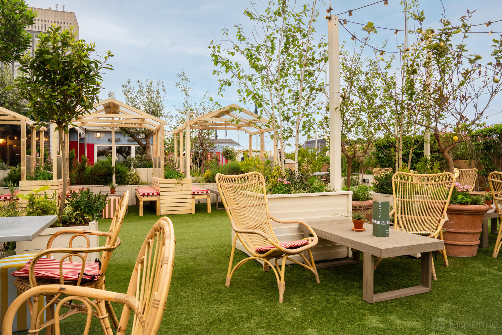 An outdoor bar with wicker chairs, wooden pergolas, and greenery on artificial grass at 1864 Rooftop Bar.