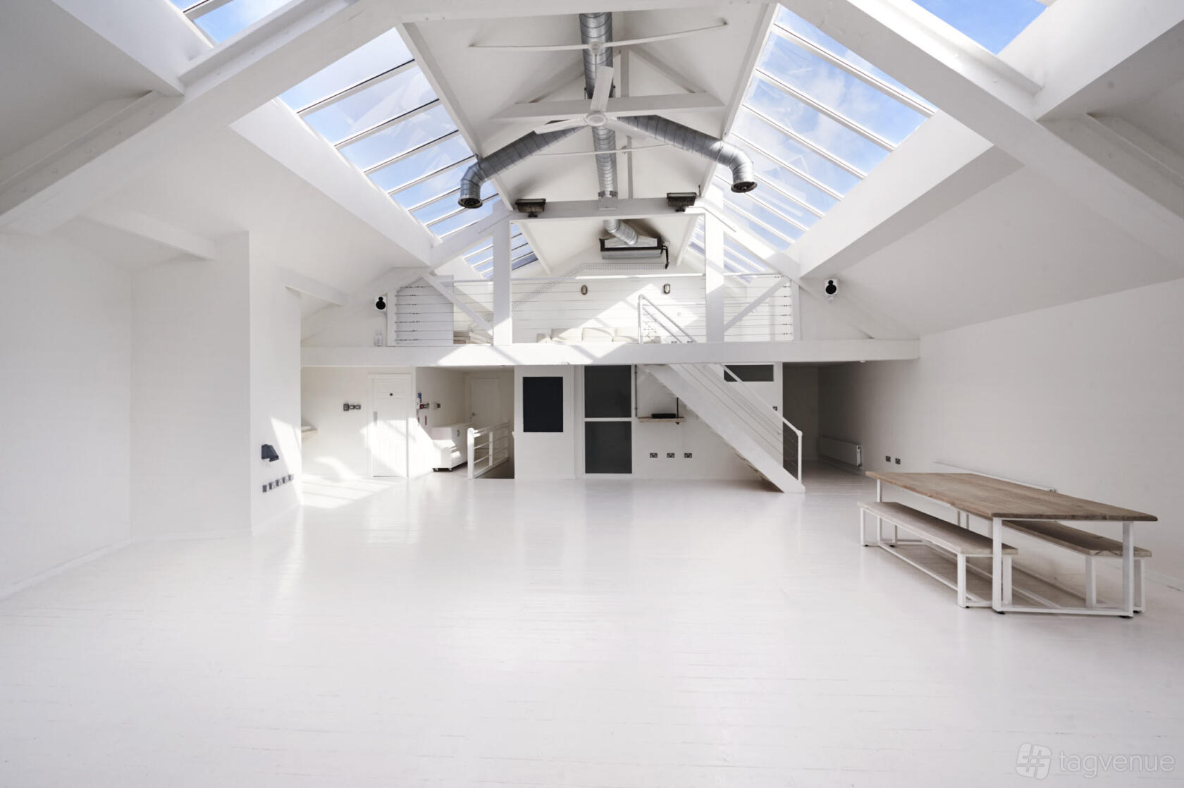 An event venue with skylights, exposed beams, white floors, and a loft area at fivefourstudios.