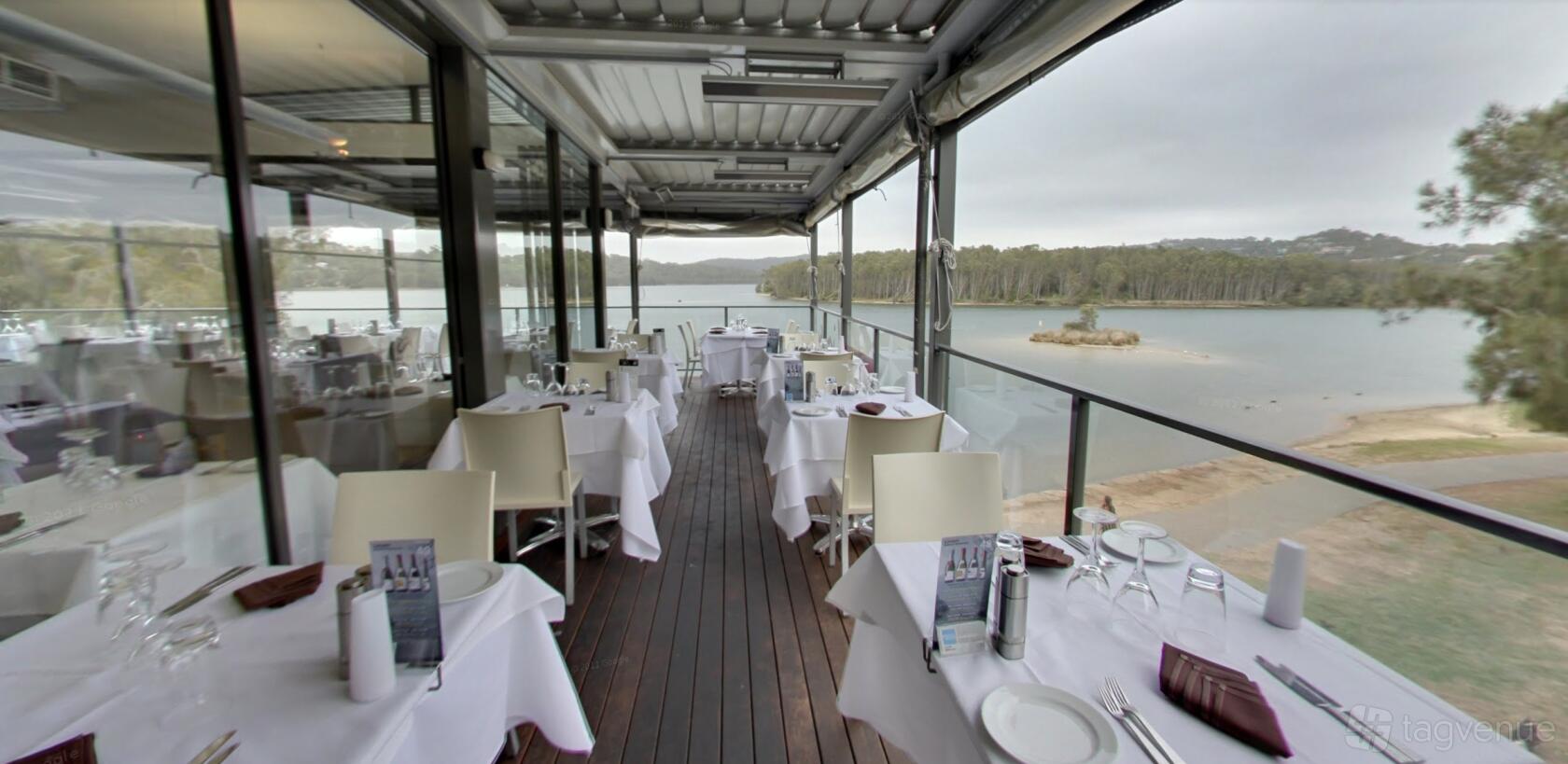 An outdoor dining area with glass walls, white tablecloths, and waterfront views at Limani Seafood Restaurant.