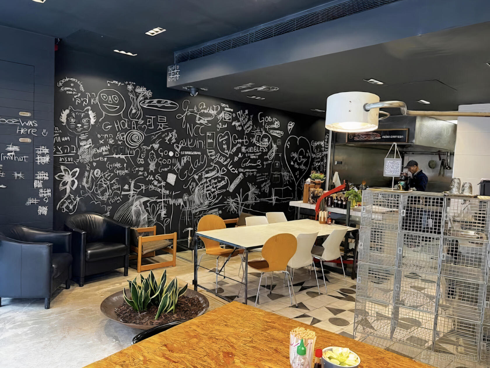 A restaurant with a chalkboard wall covered in drawings and a mix of wooden and metal chairs at G Asian Canteen.