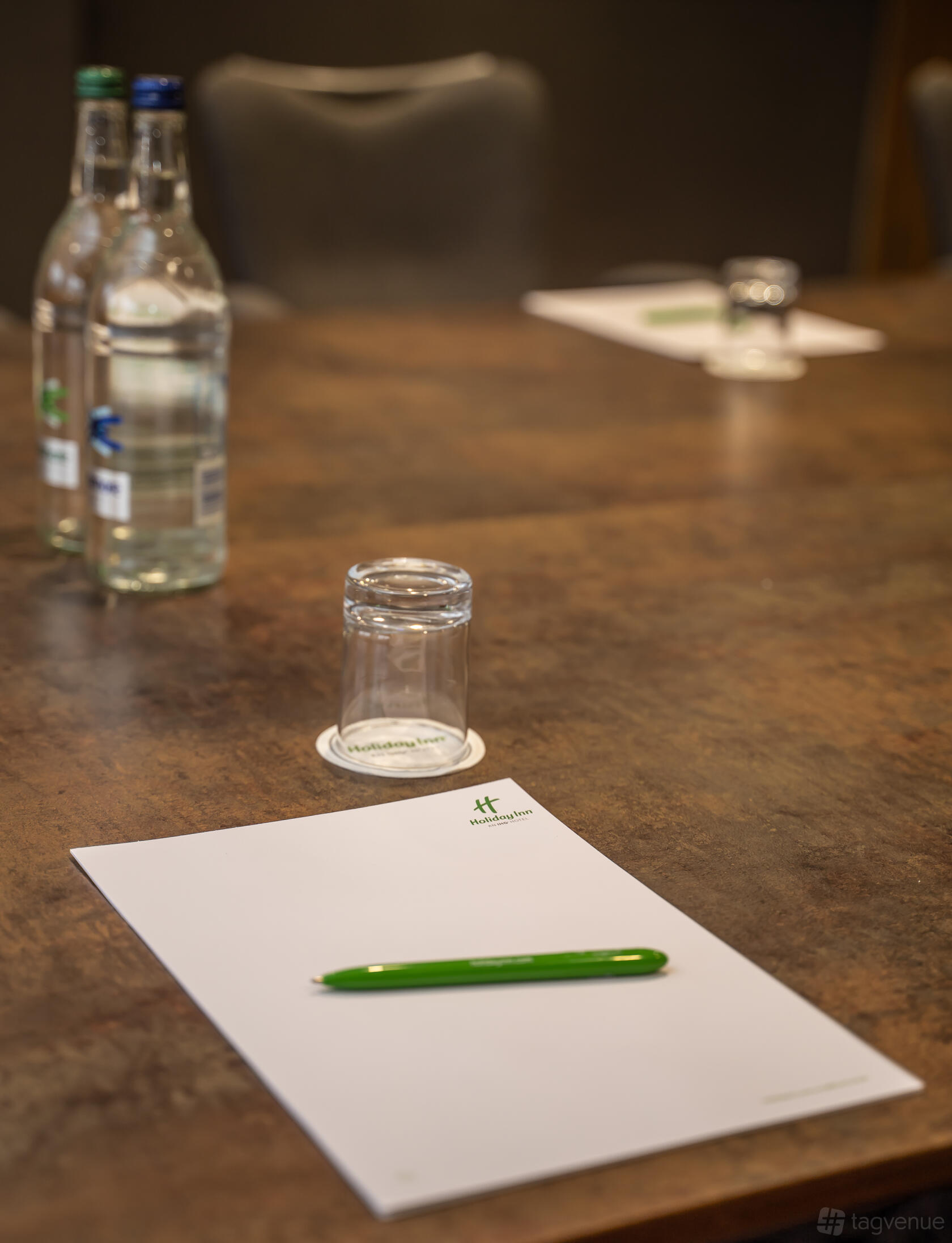 An event space with a wooden conference table set with notepads, water bottles, and glasses at Holiday Inn Leicester - Wigston.