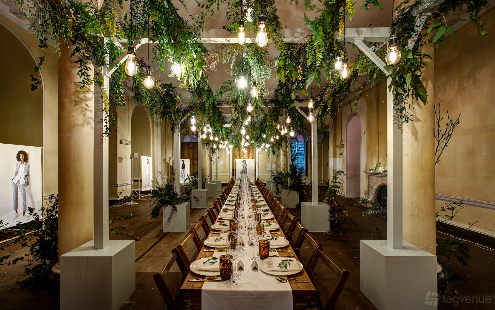 An event venue with long banquet tables, draped greenery, hanging bulbs, and tall arches in the Lancaster Room at Somerset House.