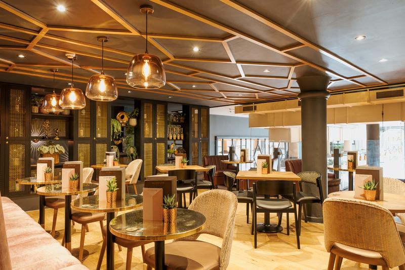 An event space in a bar with pendant lighting, gold-accented shelving, and potted plants at All Bar One Cannon St.