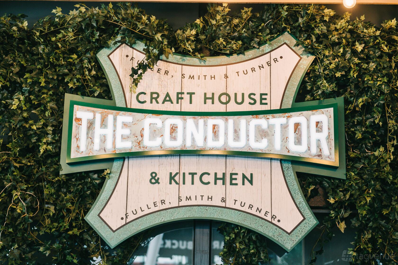 A pub event space sign with illuminated lettering and surrounding greenery at The Conductor.