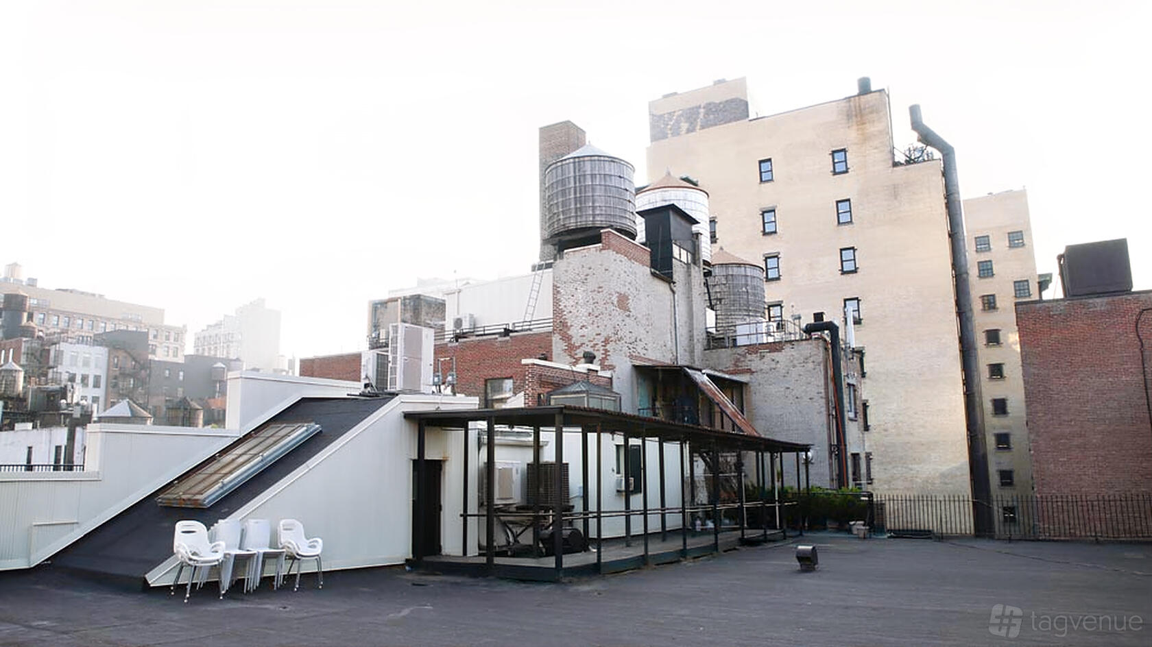 A loft rooftop with black flooring, industrial water towers, glass-walled structure, and city views at Union Square Loft.