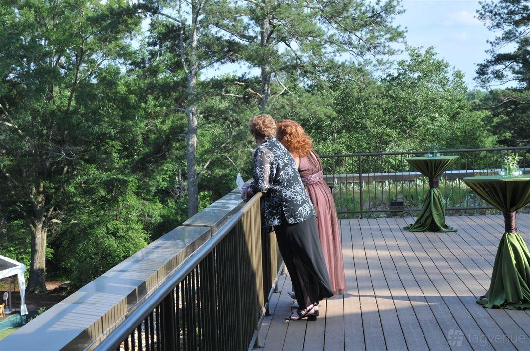 A rooftop event space with a wooden deck, cocktail tables draped in green linens, and forest views at Chattahoochee Nature Center.