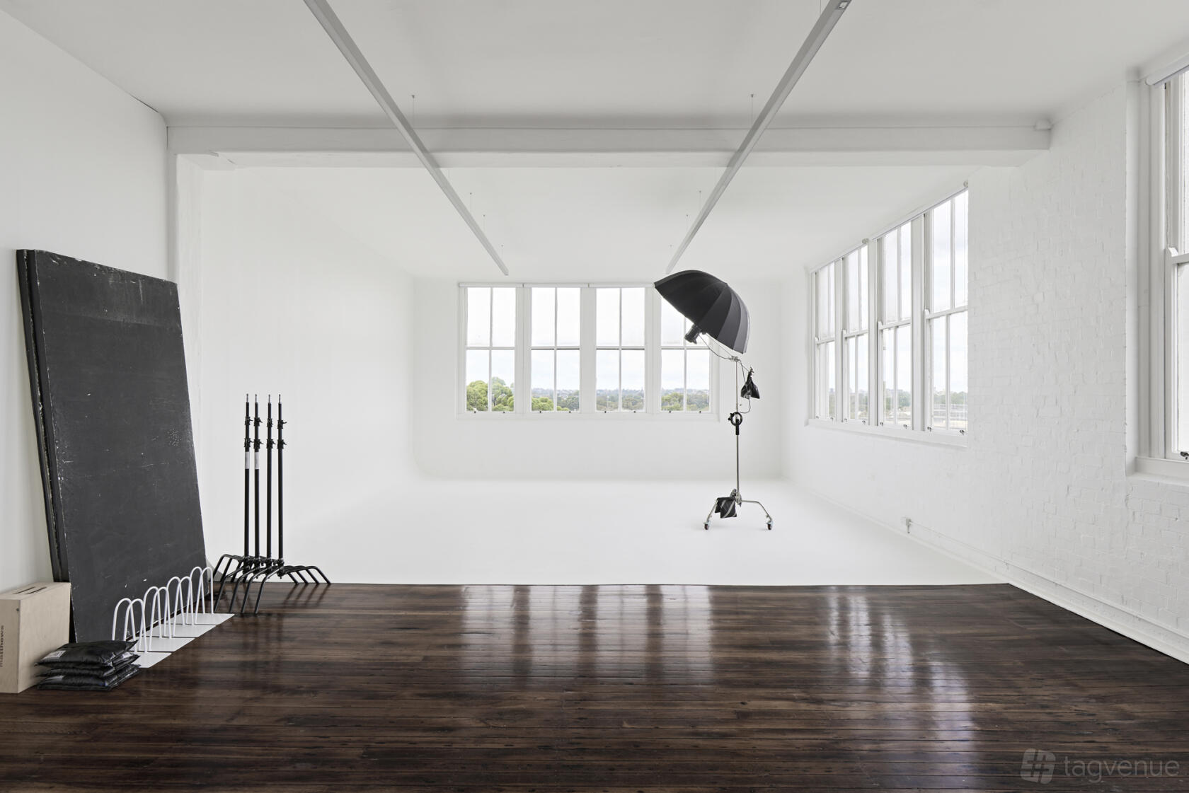 A photo studio with white walls, large windows, wood floors, and professional lighting equipment at Kinfolk Studio.
