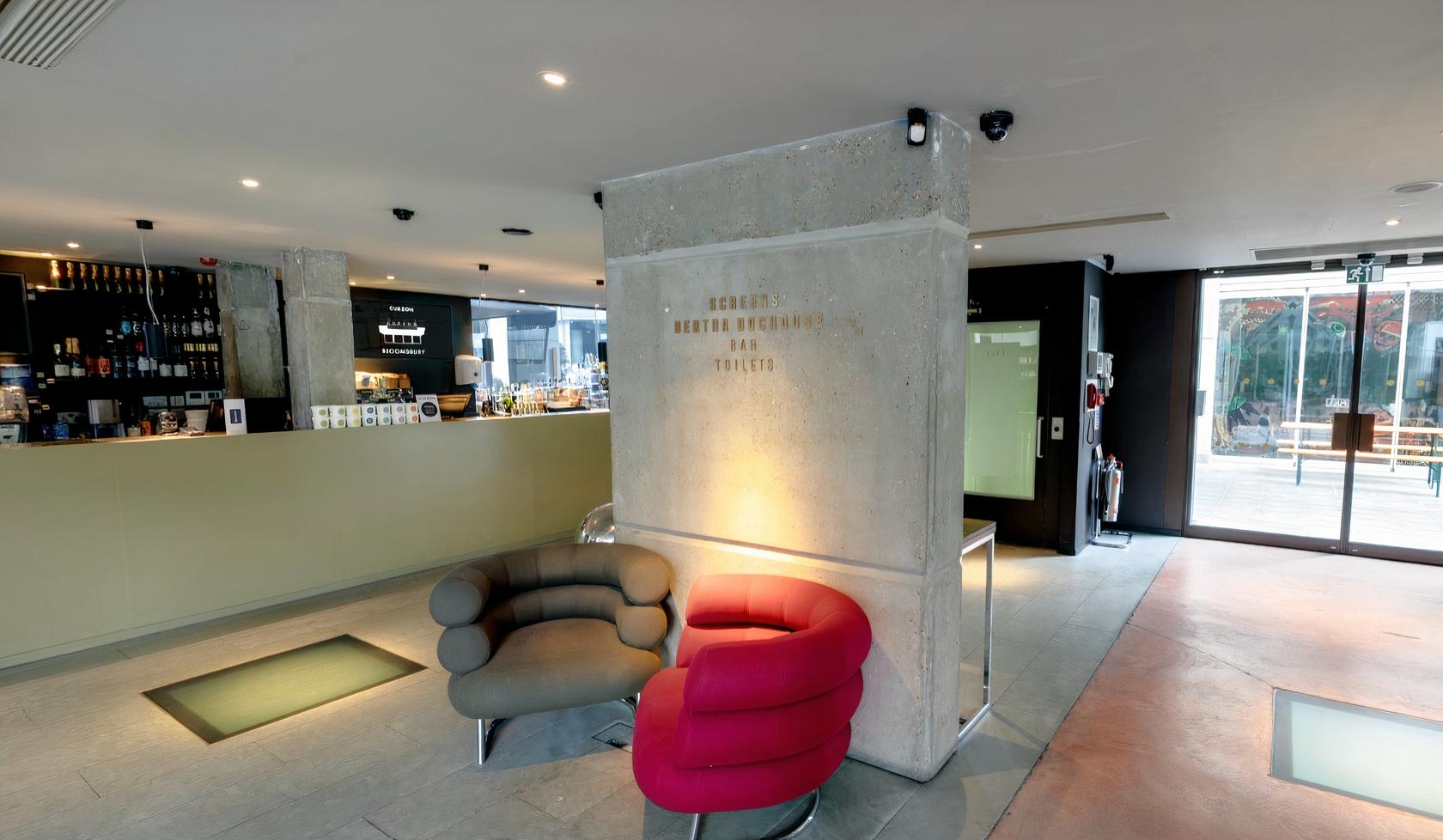 A cinema lounge with contemporary armchairs, a concrete pillar, and a sleek bar at Curzon Bloomsbury.