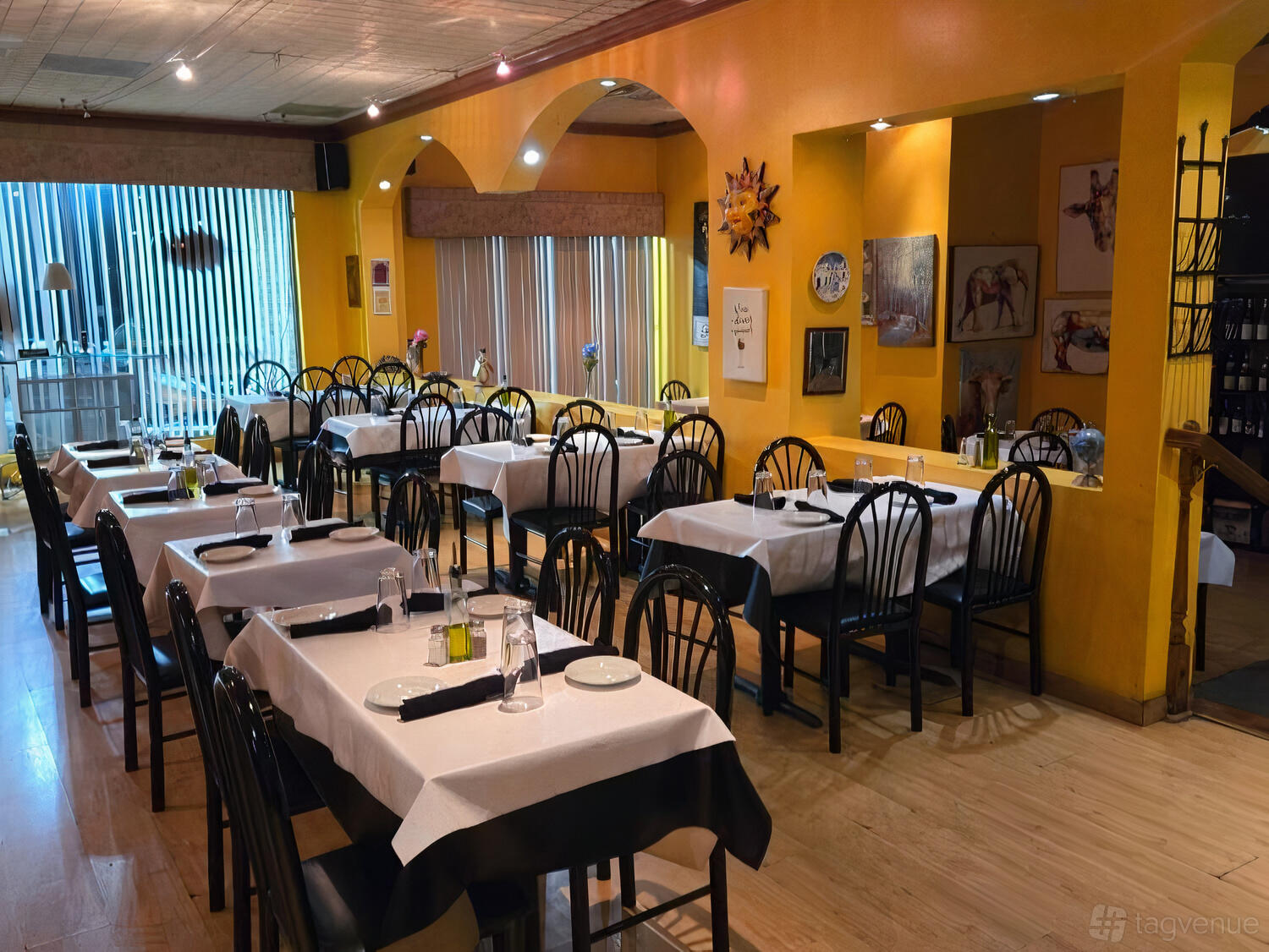 A restaurant dining area with yellow walls, black chairs, and tables set with white linens at Idylwood Grill & Wine Bar.