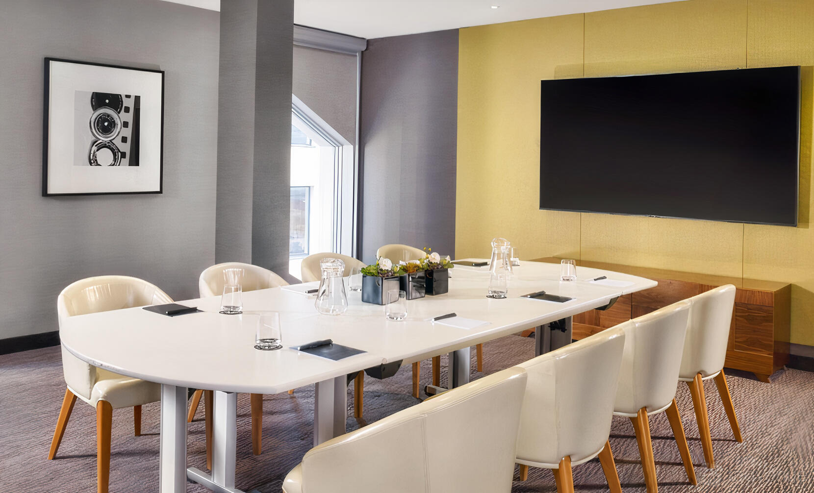 A boardroom with a glossy white conference table, white chairs, and a large wall-mounted screen at Marlowe.