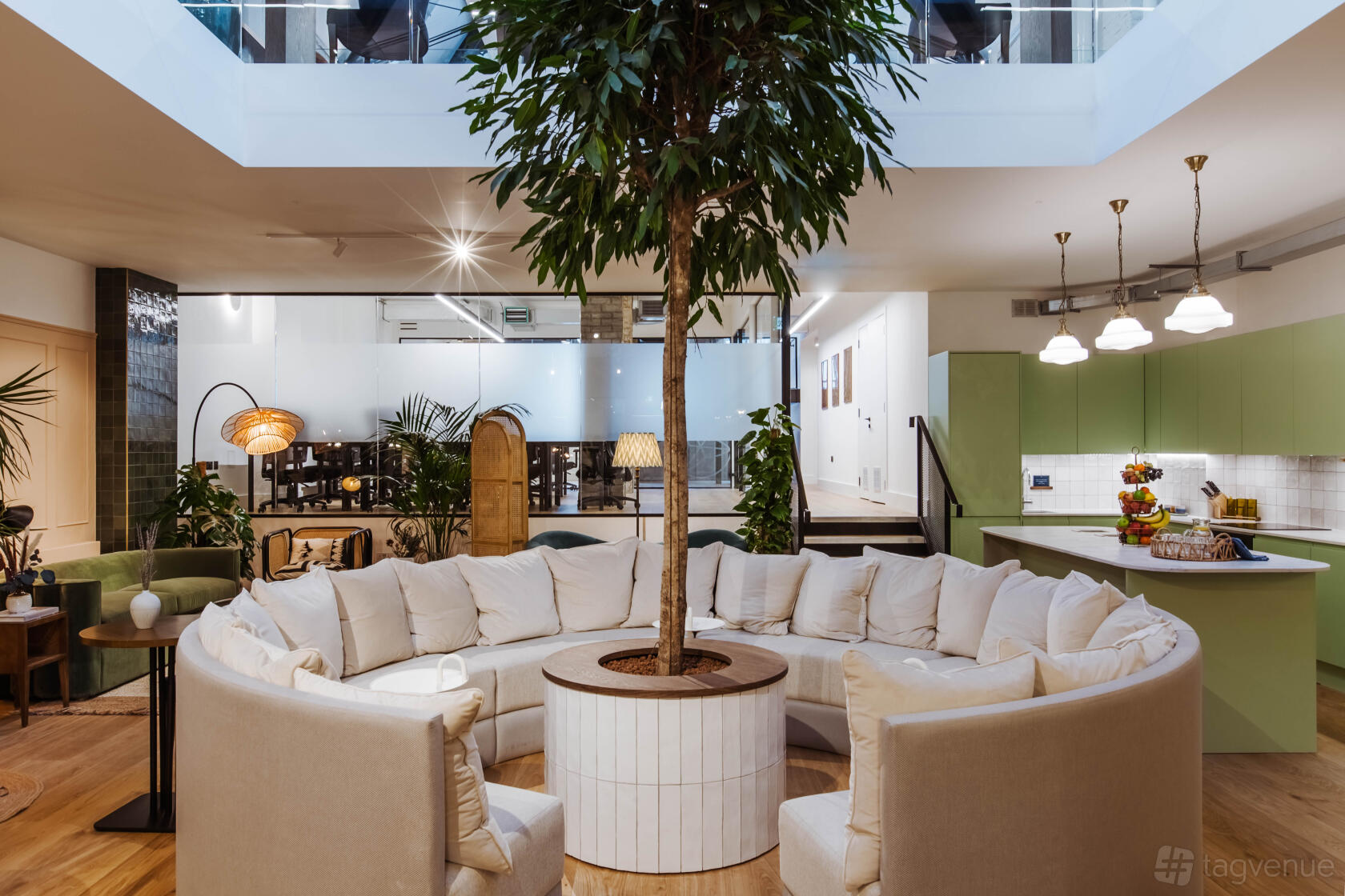 An event space with a large circular sofa around an indoor tree and natural light at Missionworks.
