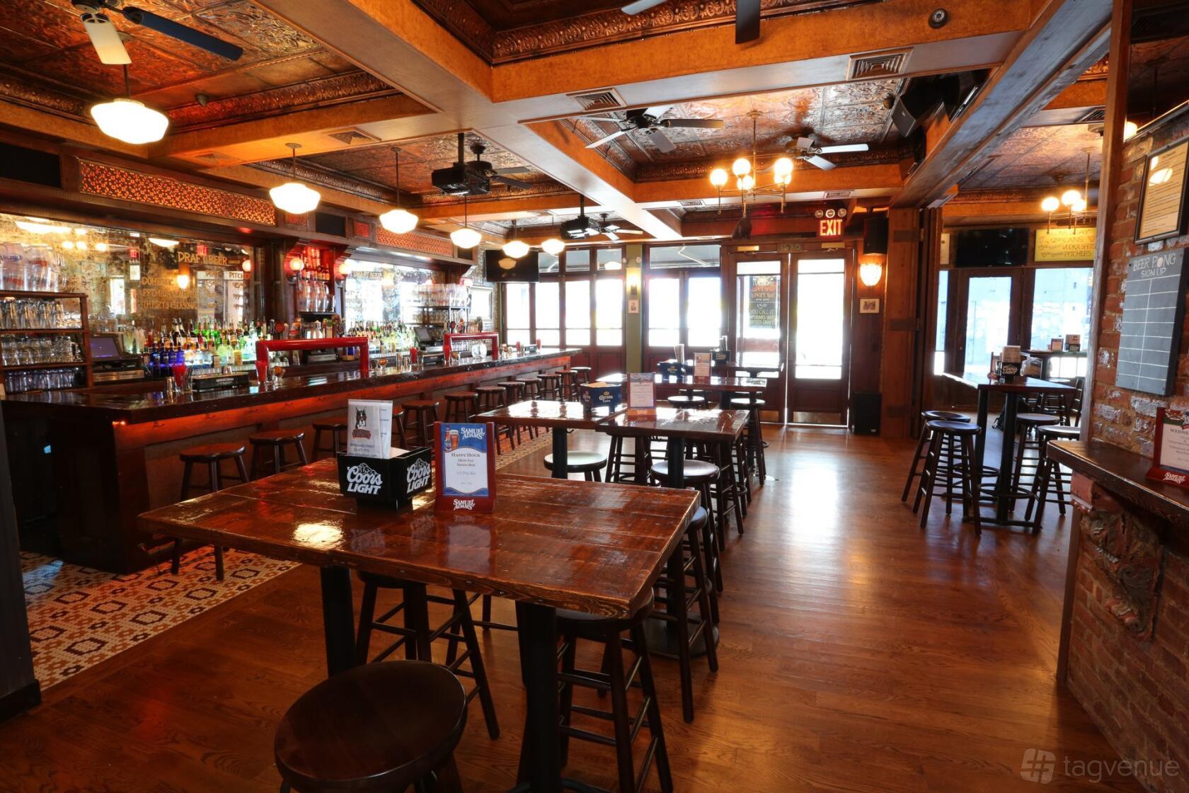 A pub with wooden tables, high stools, a long polished bar, and decorative ceiling panels at Hair of the Dog.