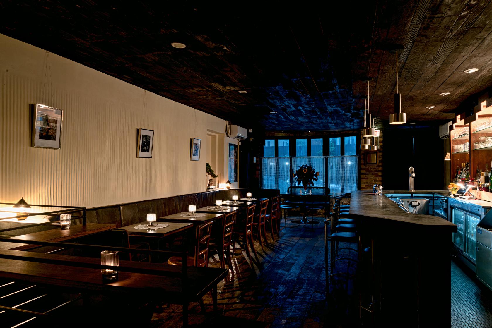 A bar with candlelit tables, wooden seating, and a long counter with barstools at Singers.