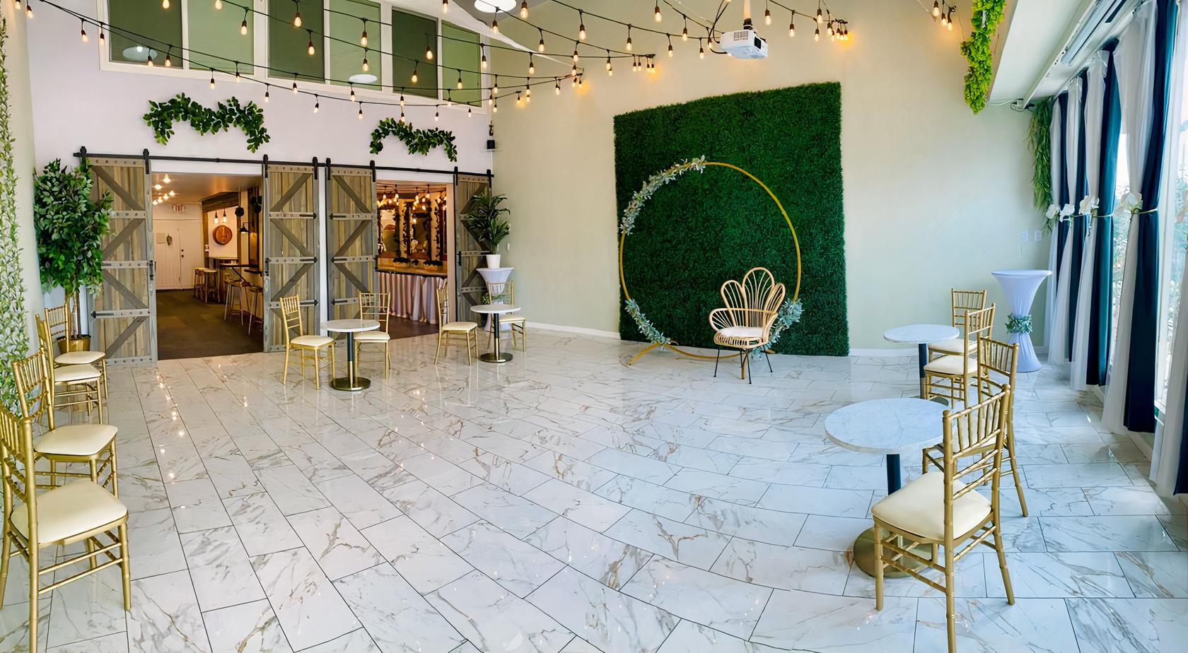 An event venue with marble flooring, string lights, a greenery accent wall, and gold chairs at Violet Cactus Studio Venue.