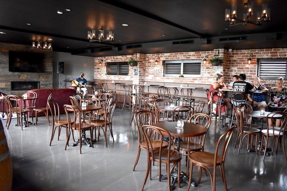 A pub interior with exposed brick walls, wooden chairs, small round tables, and ceiling chandeliers at Hogan's Wellington Point.