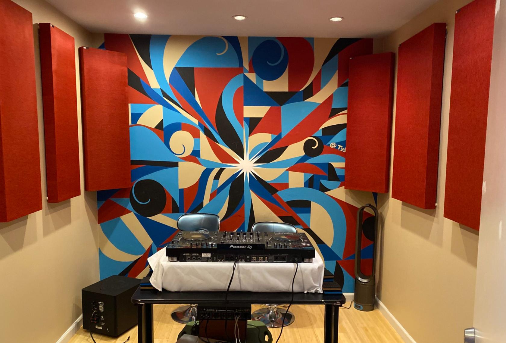 A recording studio with vibrant acoustic panels and a DJ mixing console in front of a colorful mural at The Music Company.