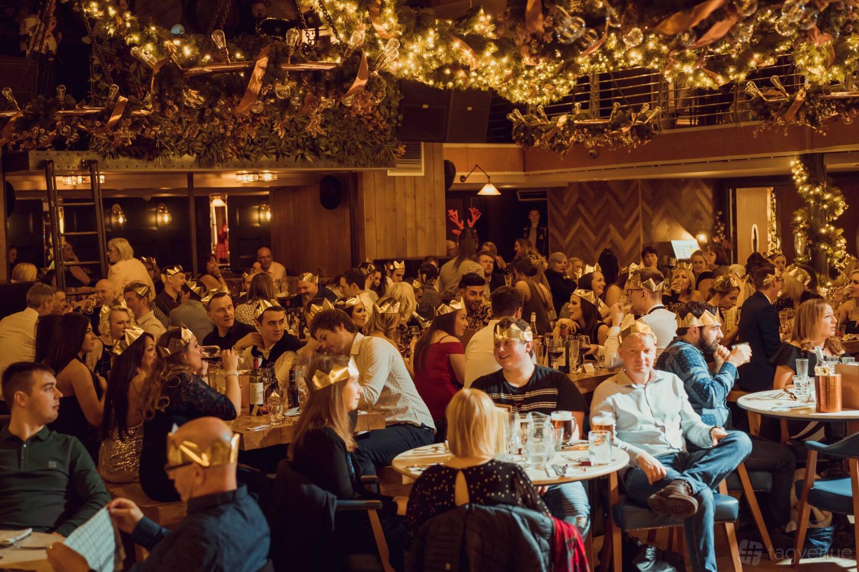 An event space in a restaurant with round wooden tables, festive string lights, and ceiling greenery at Brewhemia.