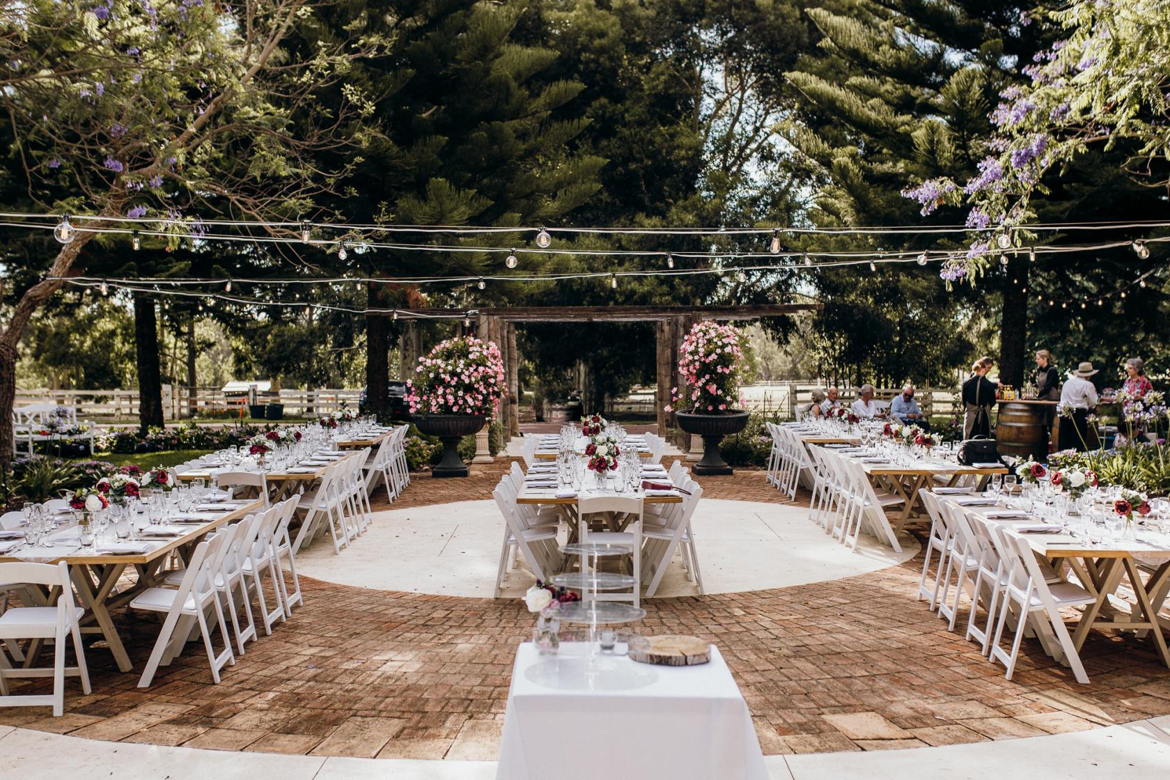 An outdoor hotel venue with long banquet tables, white chairs, floral centerpieces, and string lights at Brookleigh Estate.